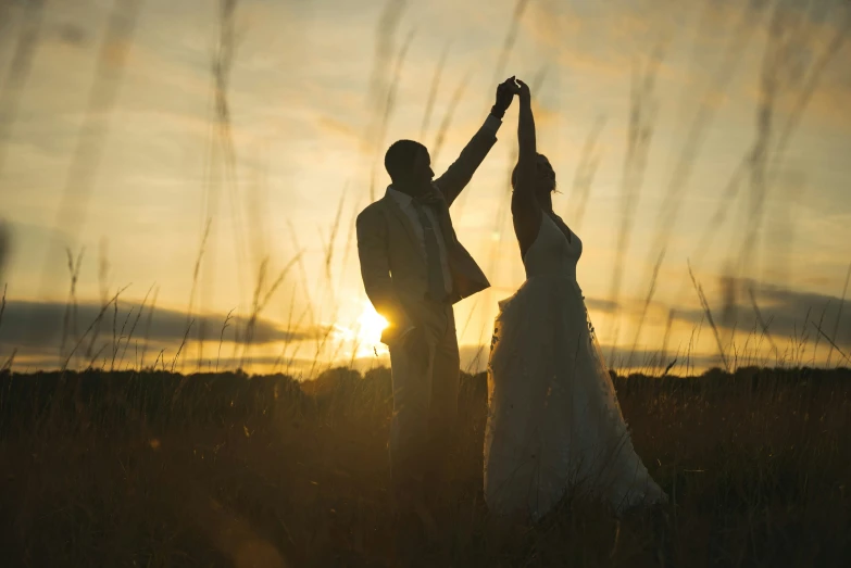 the silhouette of two brides in a field with the sun rising