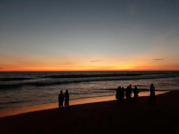 four people standing on the beach watching the sun set