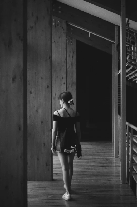 a woman walking down a hallway under wooden stairs