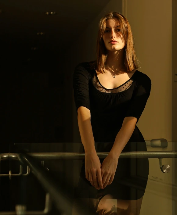 a beautiful woman wearing a black dress leaning against a glass railing