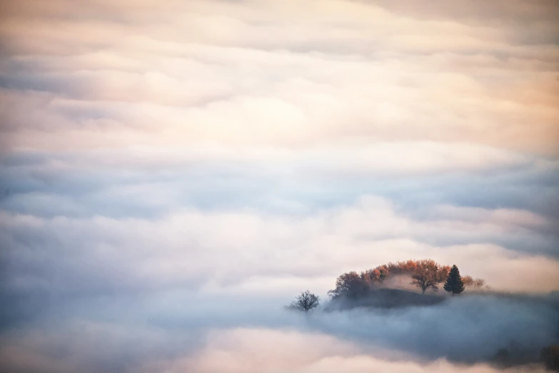 an island sitting in the middle of clouds with trees below