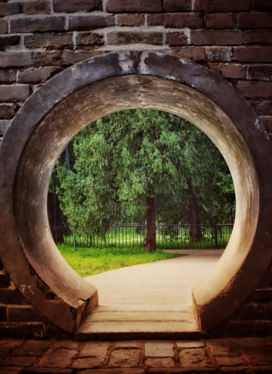 an archway in a brick wall with trees and grass