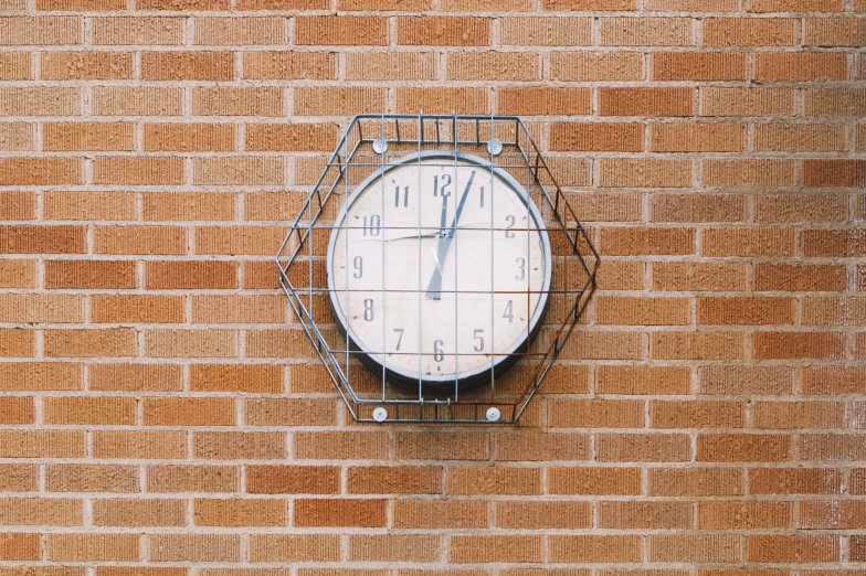 the clock is made of wire and is on a brick wall