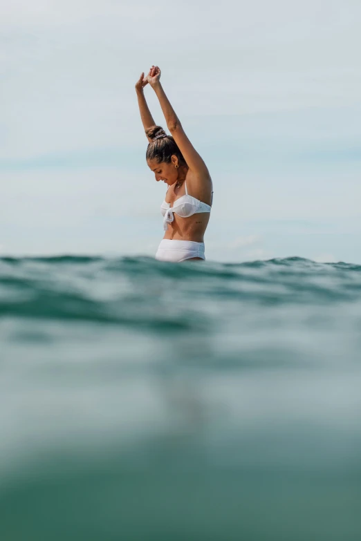 a woman stands on the edge of a body of water with her arm in the air