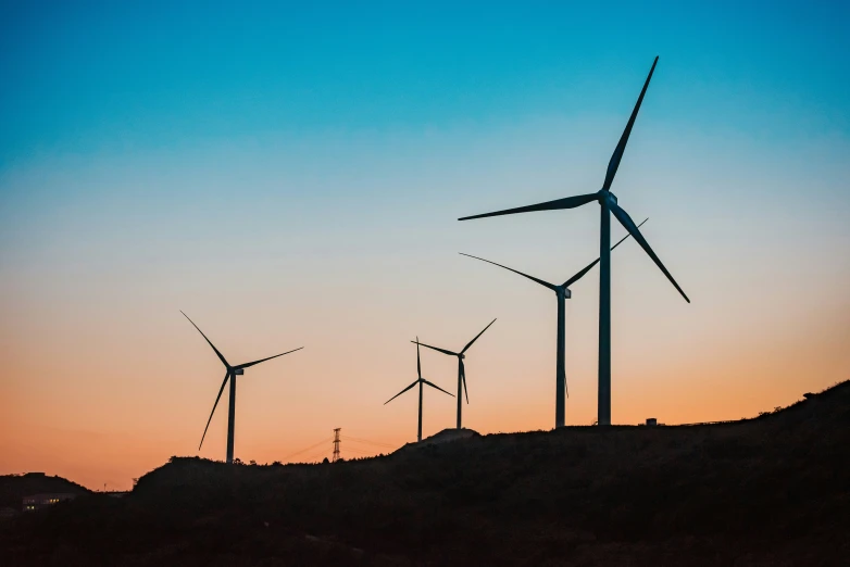 several wind turbines line the hillside at sunset