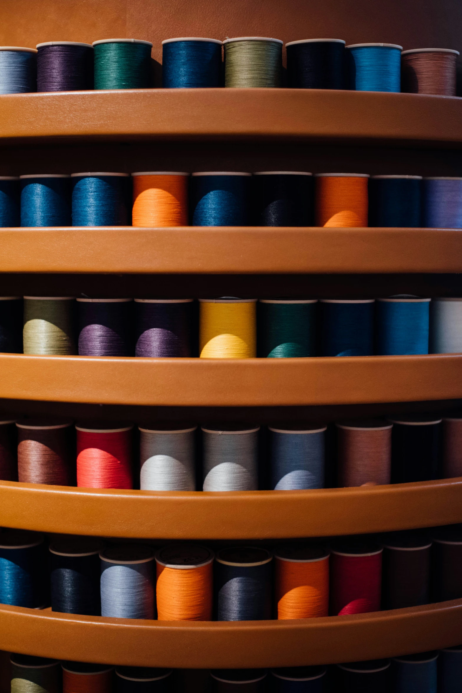 a row of wooden shelves with various colored spools of thread