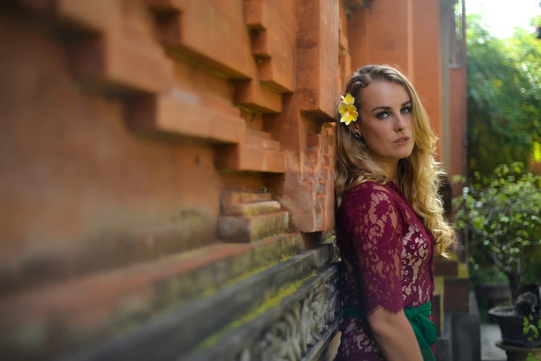 a blonde woman with a flower in her hair stands near a wall