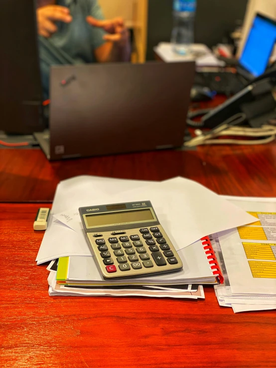 a calculator on a pile of papers in front of a laptop