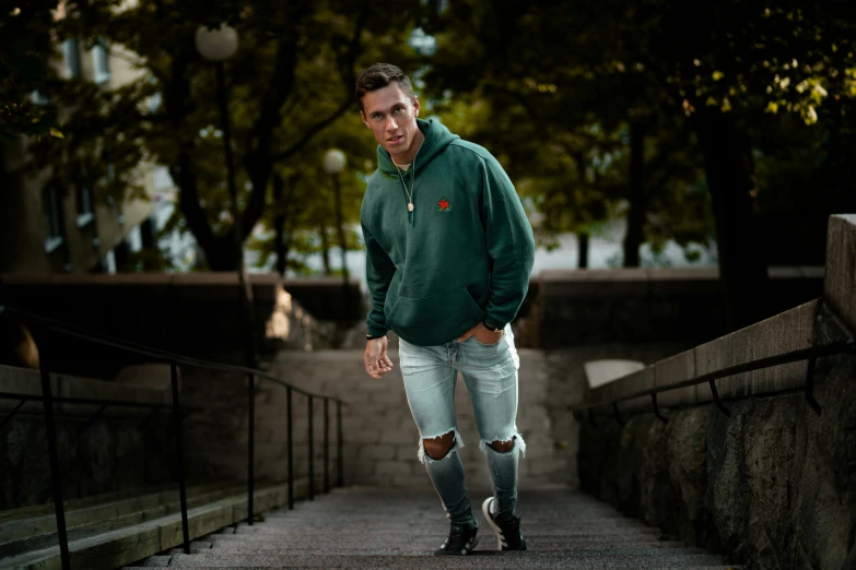 a man in green sweater and ripped jeans standing by a railing