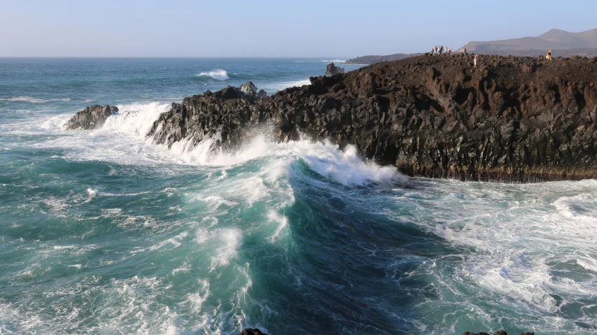 some water waves a cliff a couple people and some mountains