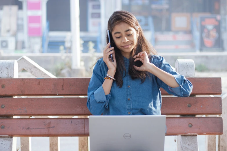 a girl on her cell phone next to a laptop on the bench