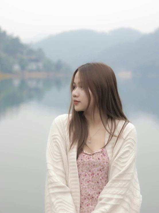 a woman wearing a long white cardigan by a lake