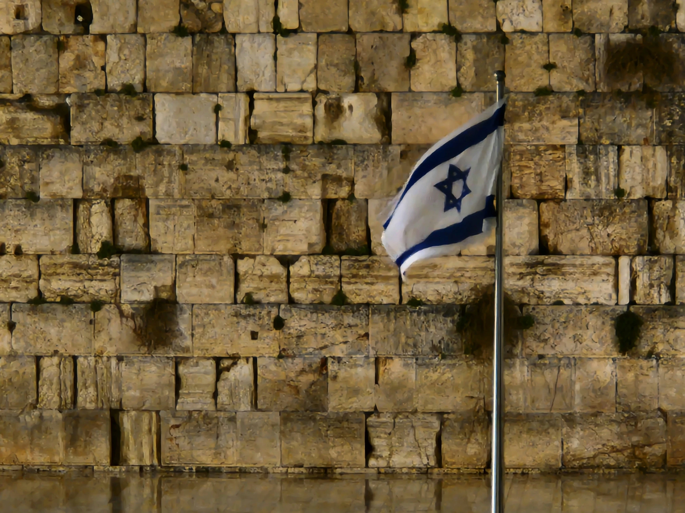 an israeli flag flying high on top of a pole near some bricks