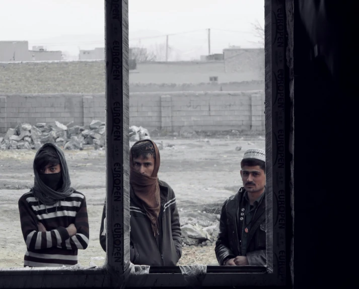 three people, including one wearing head scarves, are standing looking out windows