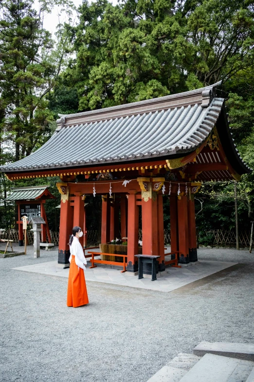 a woman dressed in orange standing by a red building