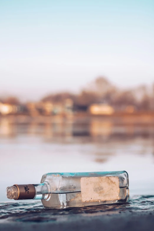 an empty bottle is sitting on the edge of a body of water