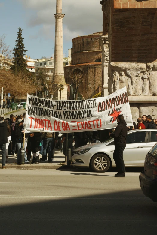protesters holding a sign while standing in front of an old monument