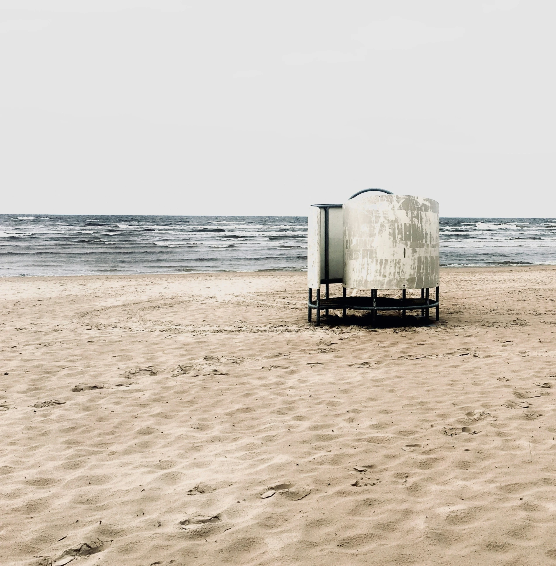 there is an empty bucket and bench sitting on a beach