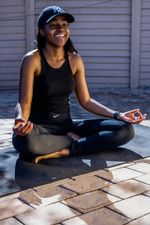 smiling woman in black top and leggings sitting on ground outdoors