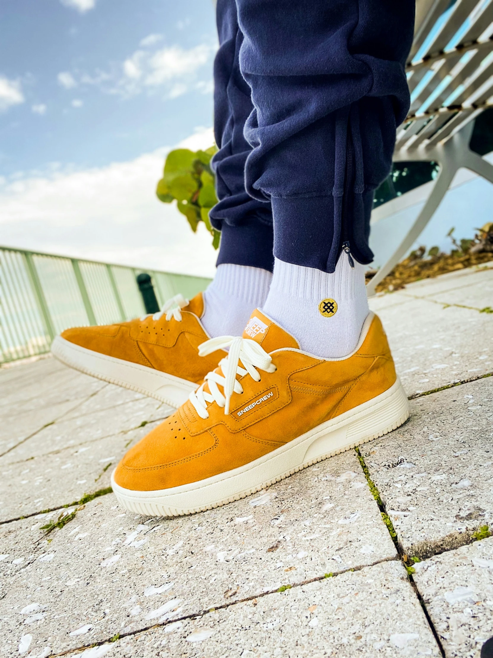 a pair of feet sitting on the pavement wearing orange trainers