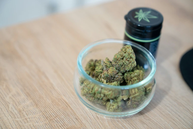 a glass jar with a marijuana strain sits on a table next to a small container of cannabis oil