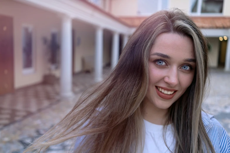 a young woman with long hair stands in front of a building and smiles