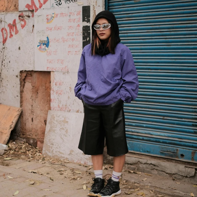 a girl stands on a street corner wearing a purple hoodie and black pleated culot skirt