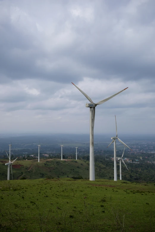 several wind turbine on a grassy hillside near a town