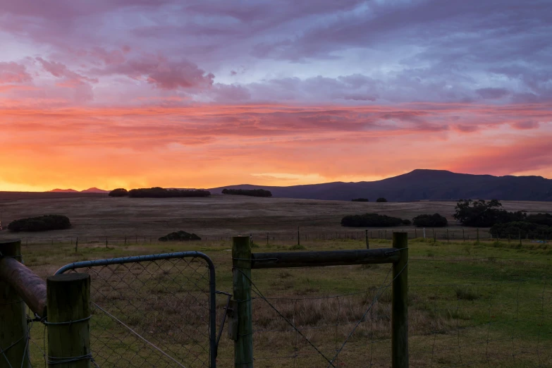 a fenced in field with a sunset over the hills