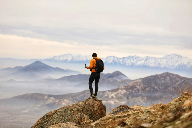person looking down at mountains with backpack and cellphone