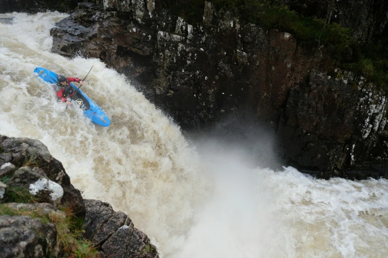 the person is kayaking along the tall waterfall