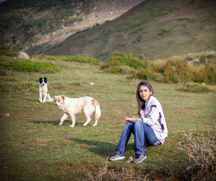 a woman sits in the grass with two dogs