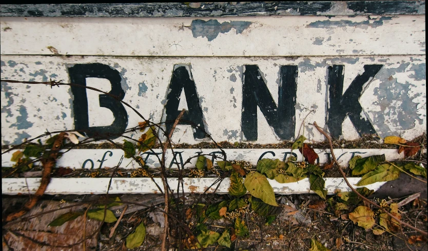 an old and rusty bank sign covered in leaves