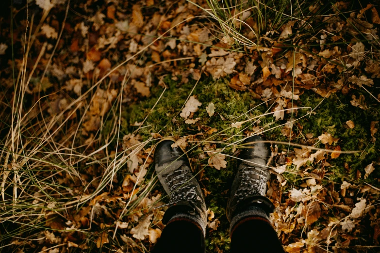 a person's feet on grass surrounded by leaves