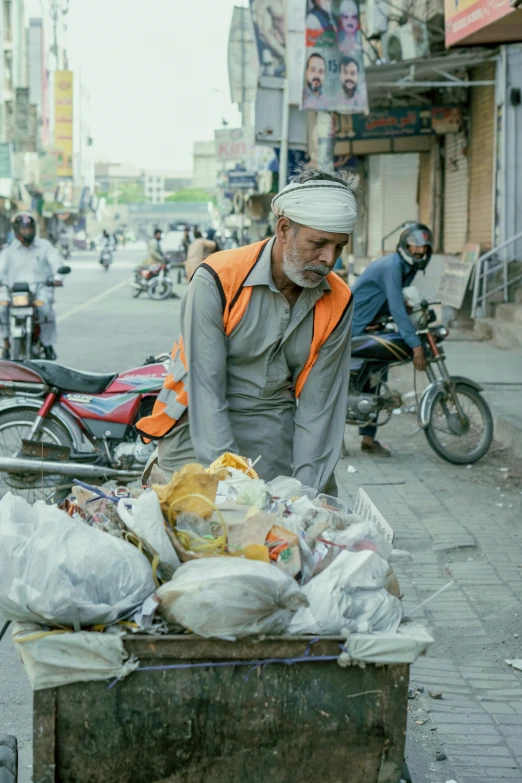 man with orange vest standing next to a cart full of bags and produce on sidewalk