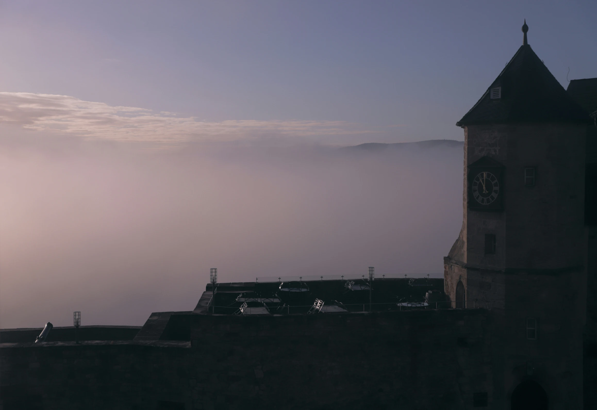 clouds roll about in the back of a medieval style tower with a clock on the front