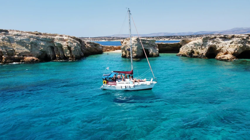 a sailboat in clear blue water with cliffs in the background