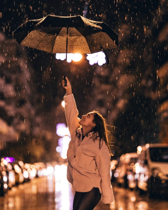 the lady is reaching up in the air to catch the umbrella