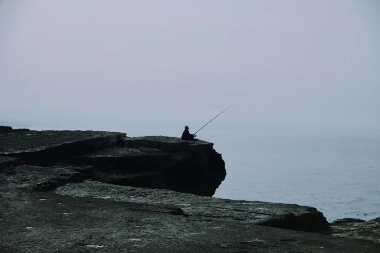 man sitting on a cliff looking out at the ocean