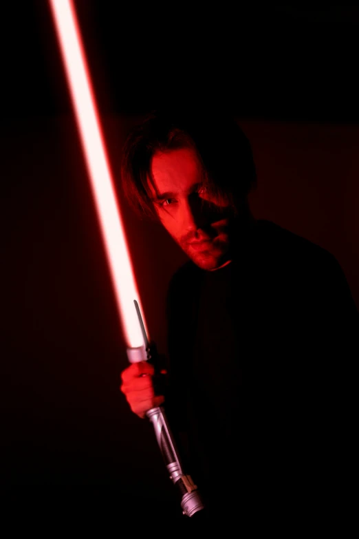 a man holding a star wars light saber in one arm and standing in the dark