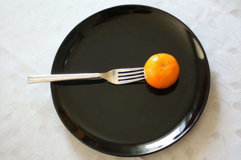 a black plate with an orange and fork on it