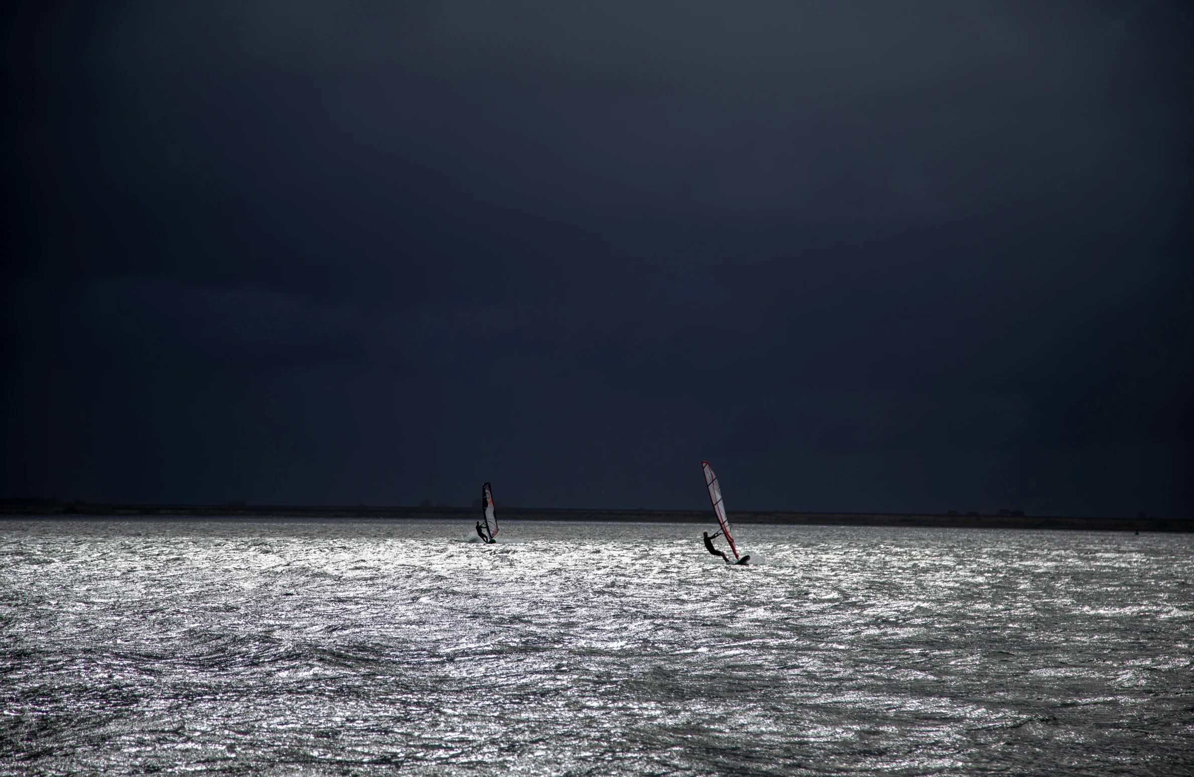 two people windsurfing on water under a dark cloudy sky