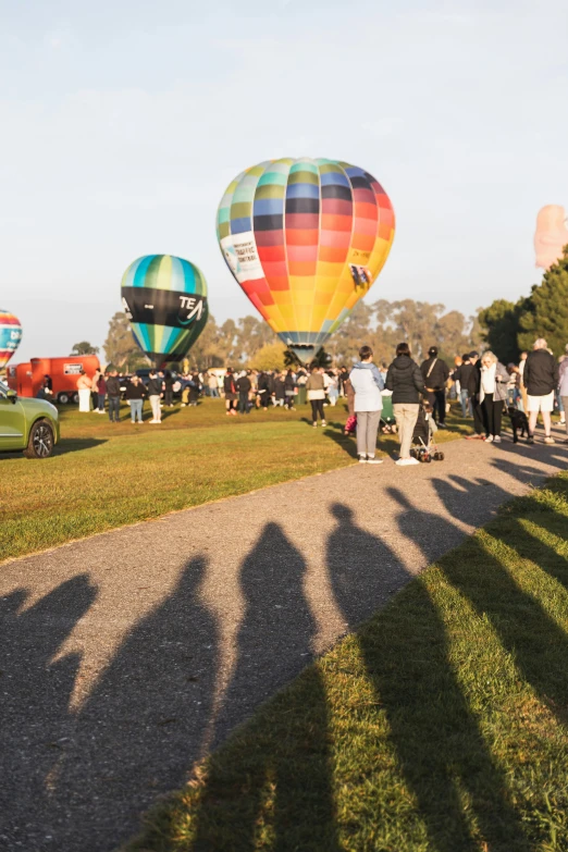 people are standing in the grass watching  air balloons