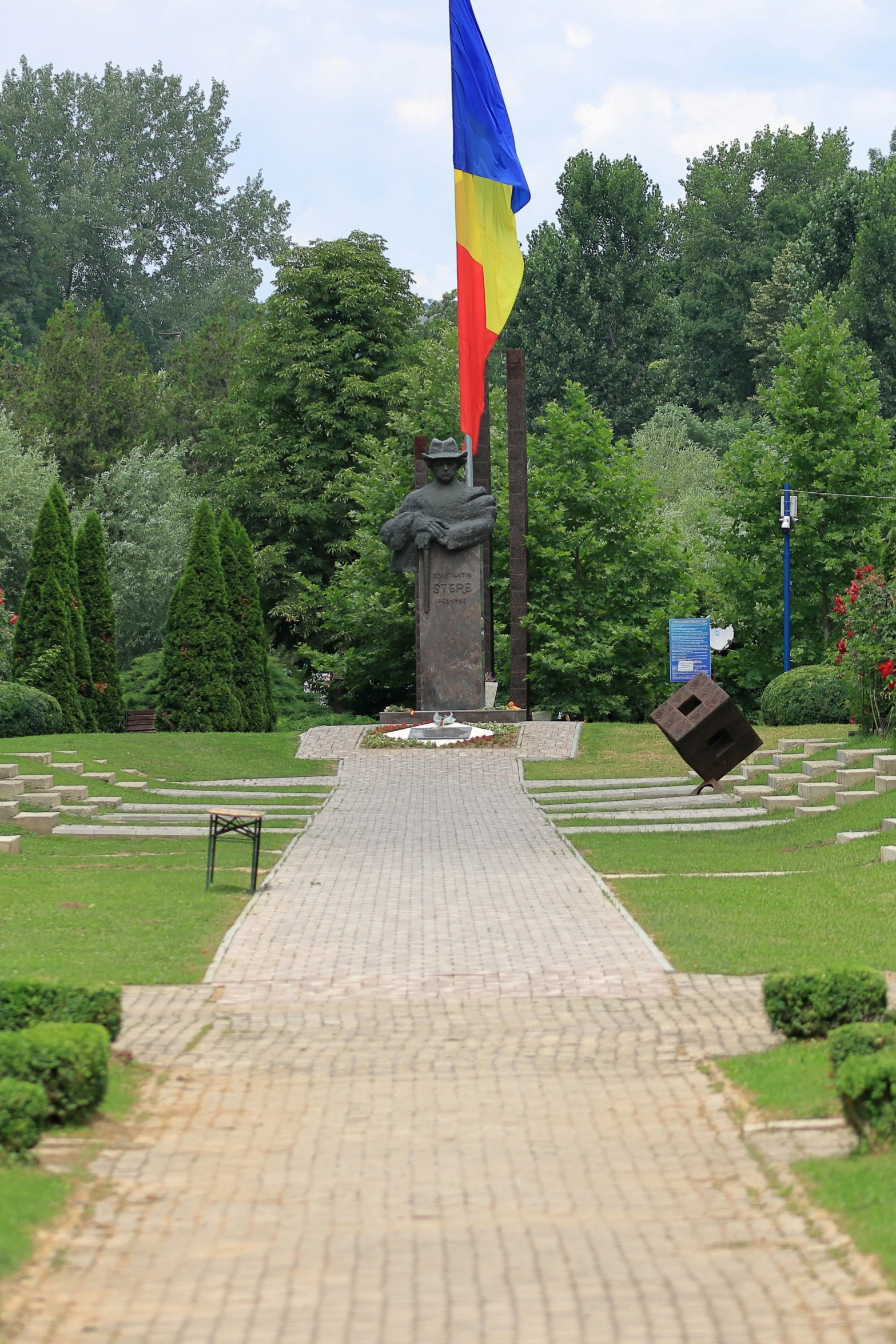 a paved path with a blue, yellow and red flag next to a statue