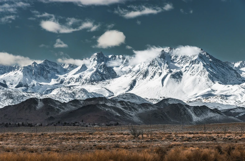 snow covered mountains sit in the distance under a cloudy blue sky