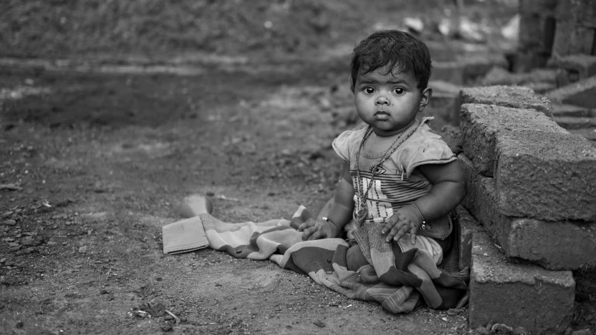 a small child sitting on a ground near brick walls