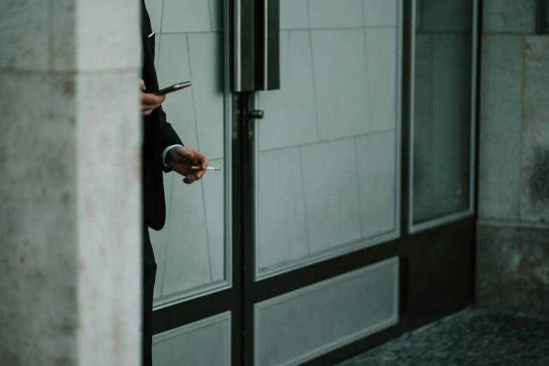 a person in a suit holding a cell phone and smoking a cigarette