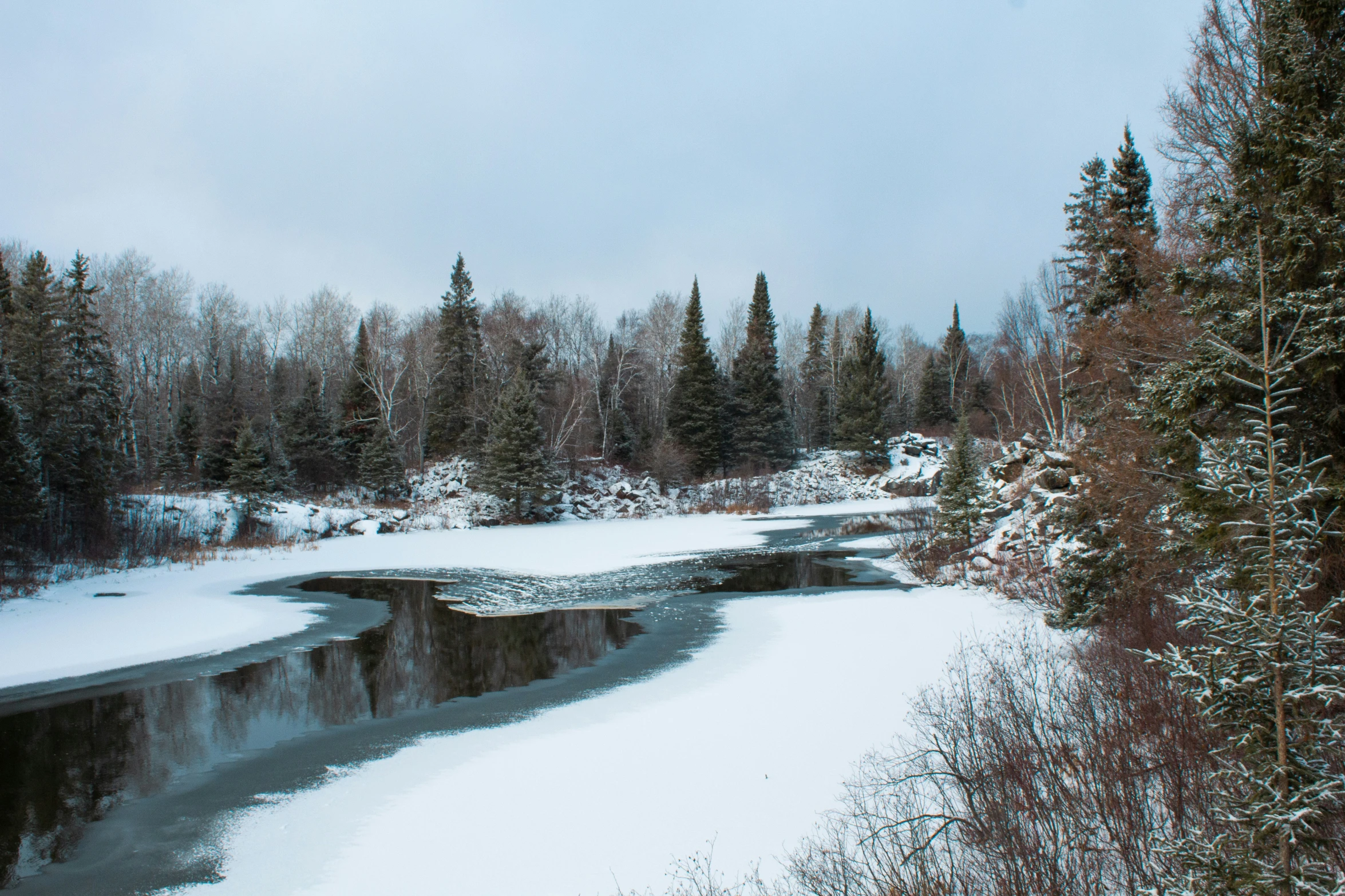 a stream running through a forest covered in snow