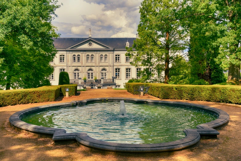 a fountain surrounded by trimmed hedges in front of a huge building