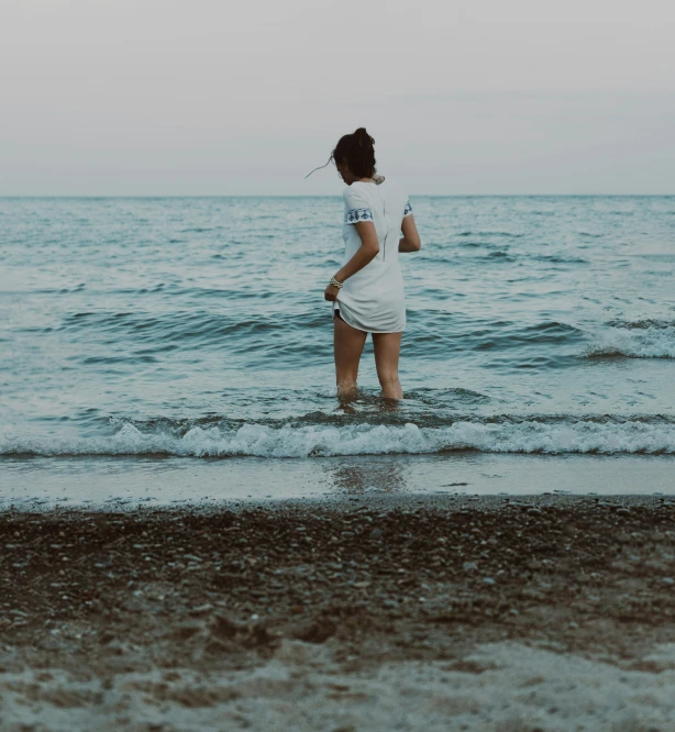 a woman stands in the ocean water, holding a cup